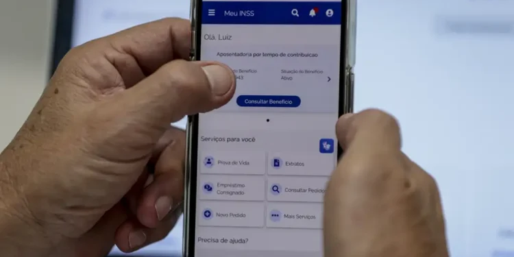 Mãos seguram celular exibindo app Meu INSS com nome Luiz, frente a notebook desfocado