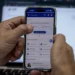 Mãos seguram celular exibindo app Meu INSS com nome Luiz, frente a notebook desfocado