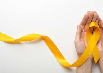 Laço amarelo encima de duas mãos com fundo branco.
