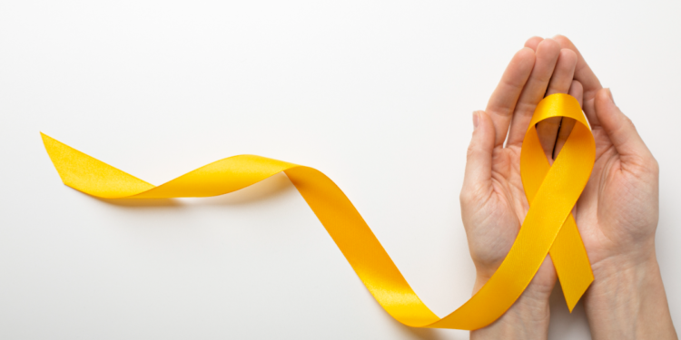Laço amarelo encima de duas mãos com fundo branco.