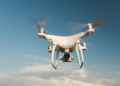 Drone quadricóptero sobrevoa céu azul em dia ensolarado.
