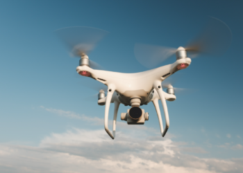 Drone quadricóptero sobrevoa céu azul em dia ensolarado.