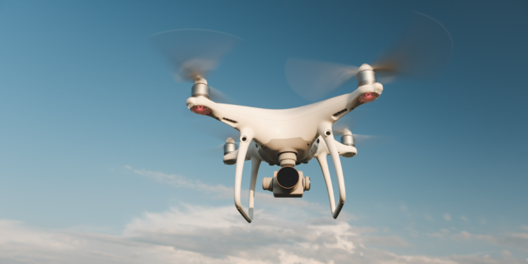 Drone quadricóptero sobrevoa céu azul em dia ensolarado.