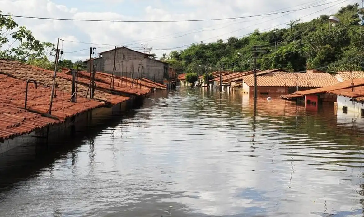 Casas com telhados vermelhos submersas em enchente, água até o teto, postes e fiação expostos