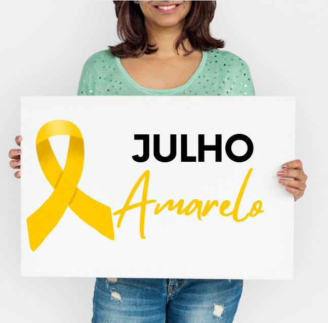 Mulher segura cartaz com laço amarelo e os dizeres Julho Amarelo em destaque.