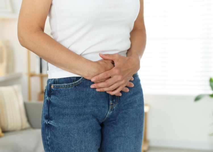 Pessoa com desconforto abdominal em ambiente doméstico.