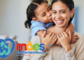 Mulher sorrindo recebe abraço carinhoso de criança e logomarca Mães de Pernambuco destaca a cena.