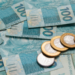 Dinheiro brasileiro em notas de 100 reais e moedas de 1 real espalhados.
