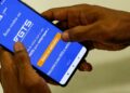 Mãos masculinas seguram celular exibindo tela do app FGTS da Caixa, botão laranja em destaque