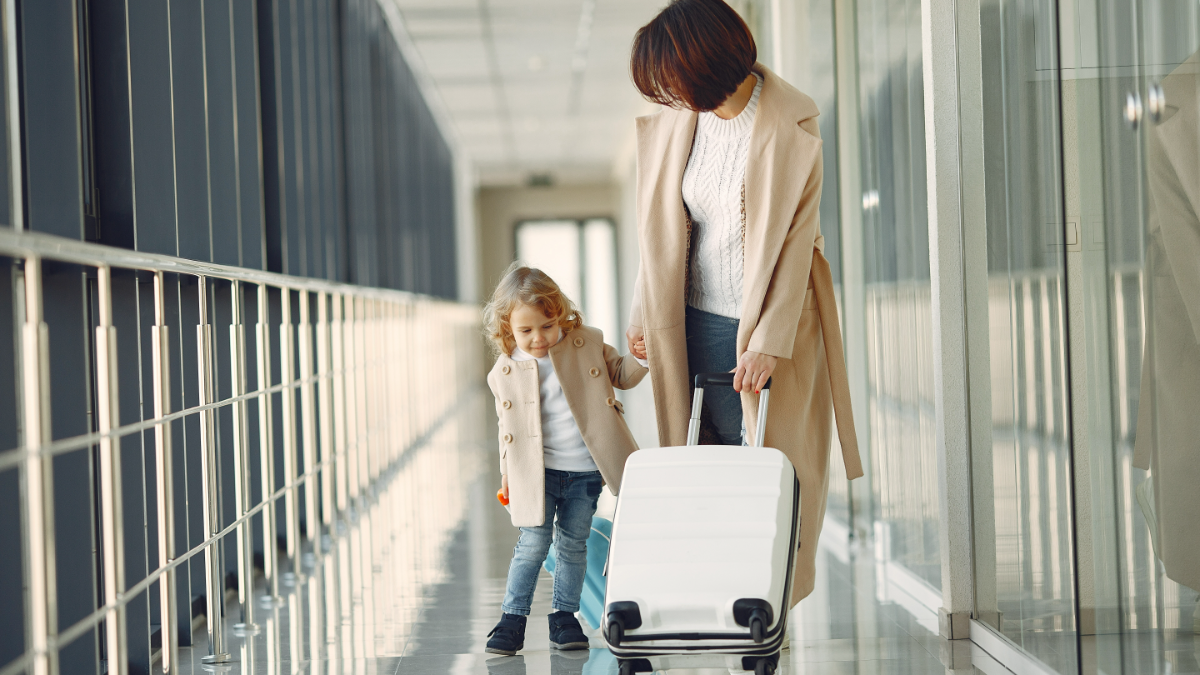Mãe e filha caminhando juntas por corredor de aeroporto moderno.