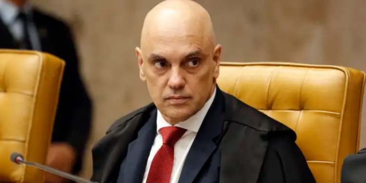 Alexandre de Moraes sentado em cadeira amarela no STF, usando terno e gravata vermelha, expressão séria.