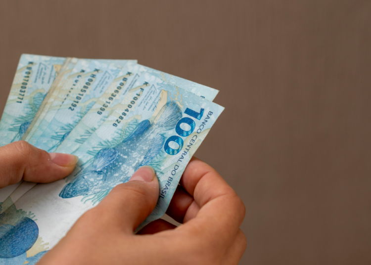Mãos segurando cédulas de 100 reais.