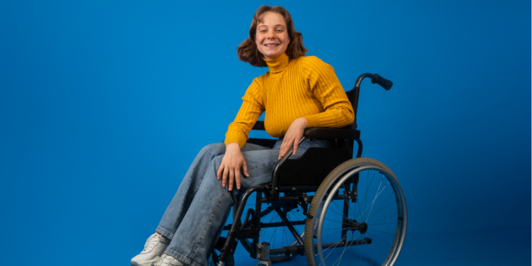 Jovem cadeirante sorridente com suéter amarelo em fundo azul.