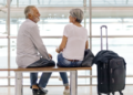 Casal de idosos conversando em banco de aeroporto moderno.