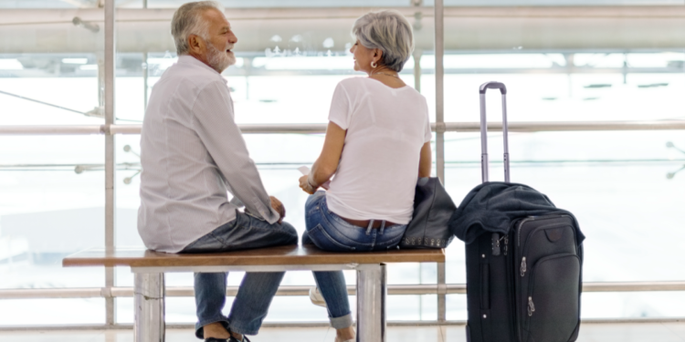 Casal de idosos conversando em banco de aeroporto moderno.