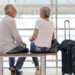 Casal de idosos conversando em banco de aeroporto moderno.