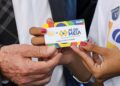Mãos segurando cartão colorido Pé-de-Meia com nome de estudante e brasão do Brasil à mostra