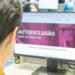 Pessoa olhando monitor com tela de autoexclusão e mensagem “pare de apostar” em escritório.