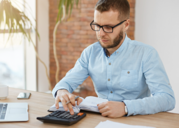 Jovem analisa finanças em escritório moderno com calculadora.