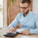 Jovem analisa finanças em escritório moderno com calculadora.