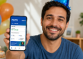 Homem sorrindo de chapéu azul segura celular mostrando saldo do FGTS em app Caixa, balões e bolo ao fundo