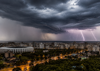 Céu escuro com nuvens densas e relâmpagos atingindo cidade de Porto Alegre e estádio em destaque