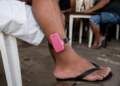 Homem com tornozeleira eletrônica rosa sentado de bermuda e chinelo em bar simples