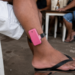 Homem com tornozeleira eletrônica rosa sentado de bermuda e chinelo em bar simples