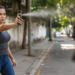Mulher jovem com expressão séria usa spray de pimenta contra pessoa em rua urbana e arborizada