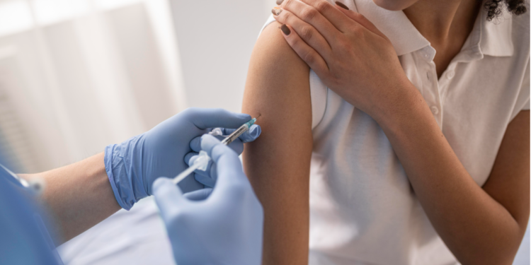 Mulher recebe vacina em consultório de saúde com profissional usando luvas.
