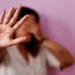 Mulher com a mão aberta à frente do rosto, palma à mostra, expressão de recusa contra fundo lilás