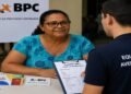 Beneficiária durante entrevista de averiguação do Cadastro Único, com a equipe preenchendo o formulário e os cartões do BPC e do Bolsa Família sobre a mesa