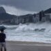 Ondas de até 3 metros atingem a orla do Rio de Janeiro durante o aviso de ressaca da Marinha, com pessoas de guarda-chuva observando o mar sob céu de chuva