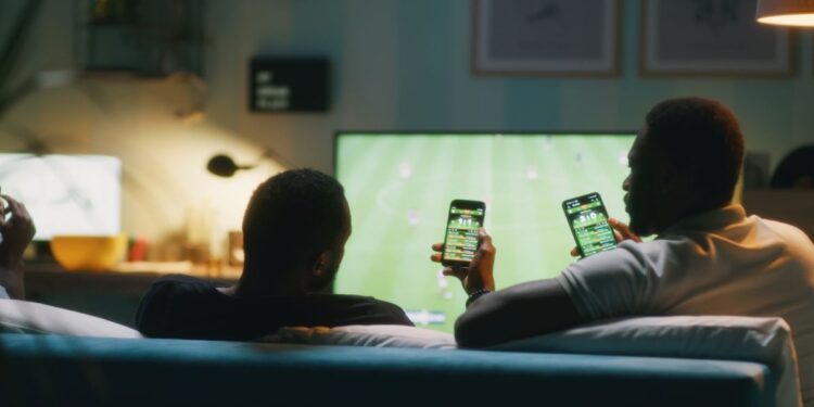 Apostadores acompanham jogo de futebol com aplicativos de apostas no celular, público atingido pelas novas regras de publicidade de bets