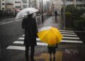 Adulto e criança com guarda-chuvas atravessando uma faixa de pedestres durante chuva forte na cidade