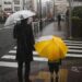 Adulto e criança com guarda-chuvas atravessando uma faixa de pedestres durante chuva forte na cidade