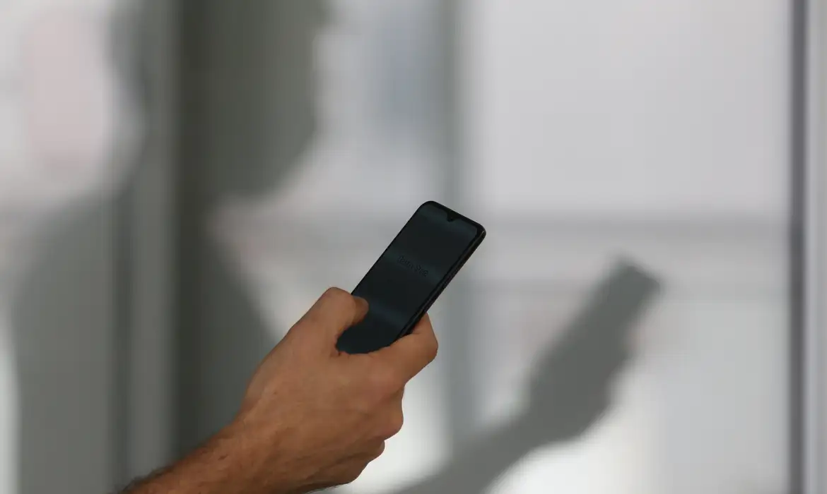 Pessoa segura o celular, tela onde os anúncios de bets passam a exibir a advertência obrigatória do Ministério da Fazenda