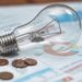 Lâmpada incandescente apoiada sobre faturas de energia elétrica ao lado de algumas moedas