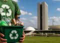 Pessoa segurando uma caixa cheia de materiais recicláveis em frente ao Congresso Nacional, em referência ao projeto que prevê desconto nas contas de luz e água para quem reciclar