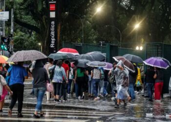Pessoas com guarda-chuvas coloridos atravessam faixa em dia chuvoso na saída do metrô República, São Paulo