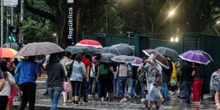 Pessoas com guarda-chuvas coloridos atravessam faixa em dia chuvoso na saída do metrô República, São Paulo