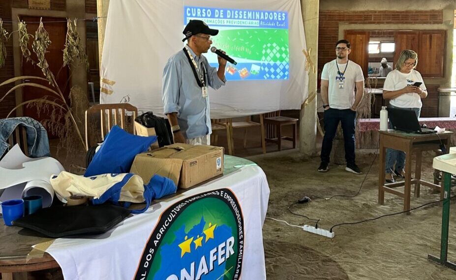 Homem fala ao microfone em curso da Conafer, com toalha estampada com o logotipo da entidade na mesa à frente