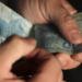 Imagem ilustrativa de mãos contando cédulas de cem reais em um fundo escuro, representando a verba destinada ao pagamento de benefícios sociais