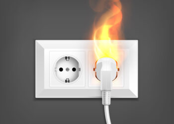 Imagem ilustrativa de tomada na parede com um plugue conectado em chamas, representando o dano a aparelhos causado por problemas no fornecimento de energia