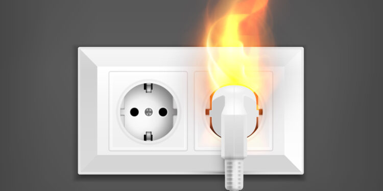Imagem ilustrativa de tomada na parede com um plugue conectado em chamas, representando o dano a aparelhos causado por problemas no fornecimento de energia
