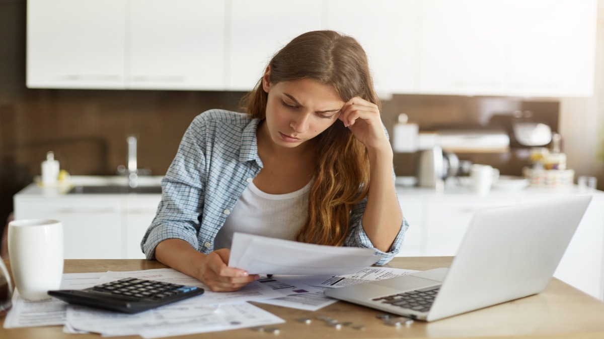 Mulher analisa contas com expressão preocupada diante do notebook e da calculadora, ilustrando a renegociação de dívidas do Desenrola Adimplentes