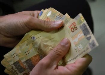 Mãos contam cédulas de 50 reais, ilustrando os juros que passam a correr durante a carência do crédito do Fies Empreendedor