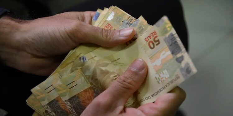 Mãos contam cédulas de 50 reais, ilustrando os juros que passam a correr durante a carência do crédito do Fies Empreendedor