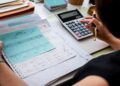 Pessoa faz contas com calculadora sobre documentos financeiros, ilustrando o crédito do Fies Empreendedor para quem quer empreender