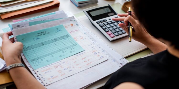Pessoa faz contas com calculadora sobre documentos financeiros, ilustrando o crédito do Fies Empreendedor para quem quer empreender